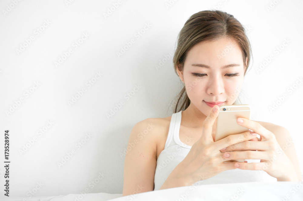 Asian beauty woman wake up and holding phone in hand in morning on bed in white bedroom Asian beauty woman wake up and holding phone in hand in morning on bed in white bedroom