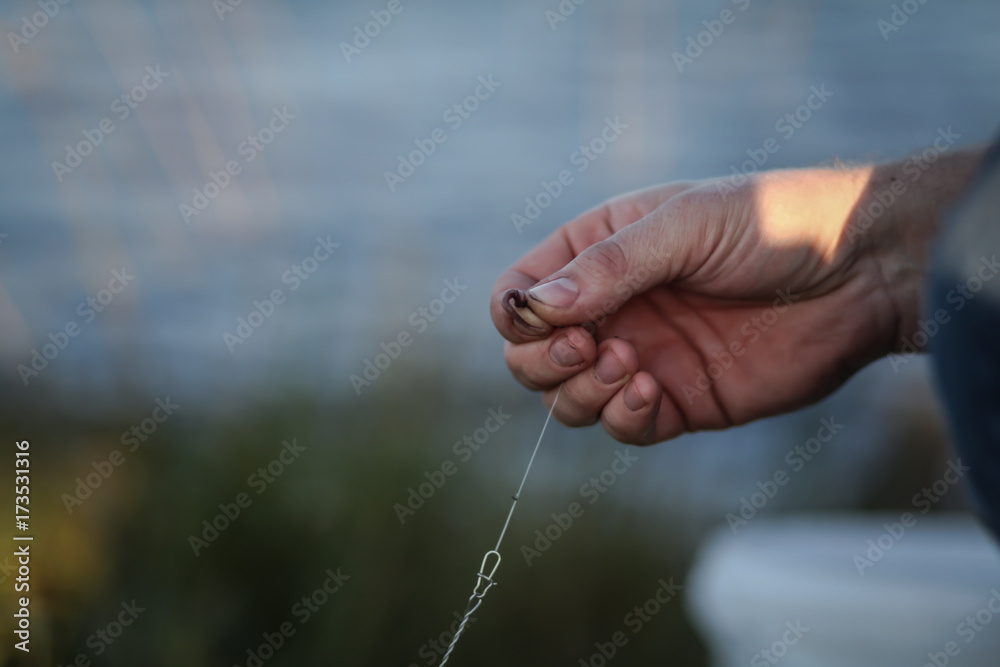 рыбак насаживает червяка на крючок на рыбалке 