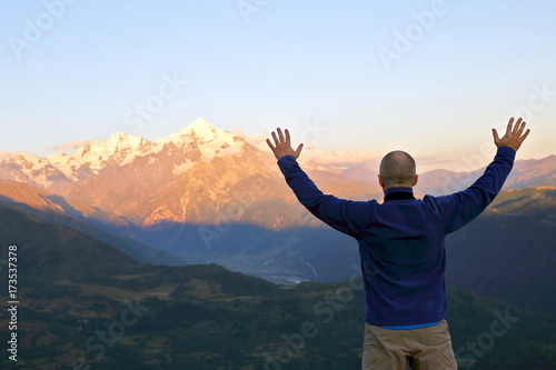 man with and raised hands standing in front of the mountains