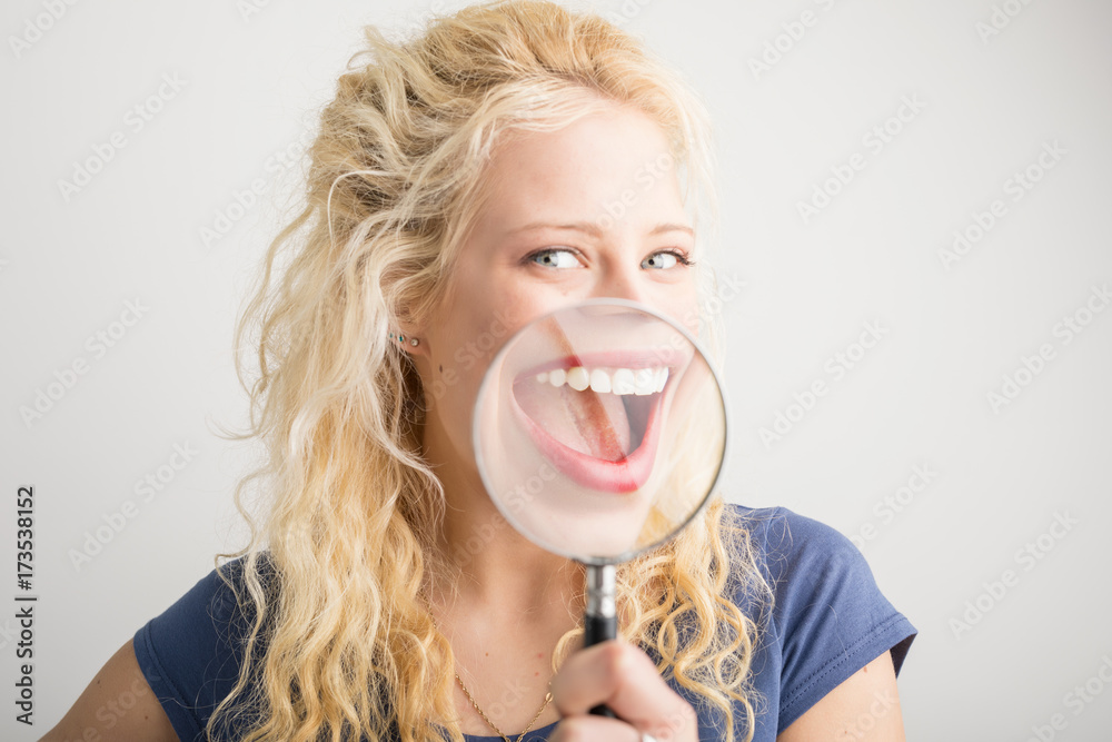 Woman showing her smile through magnifying glass - obrazy, fototapety, plakaty 