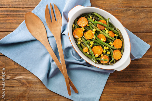 Casserole dish with delicious green beans, corn and carrot slices on table