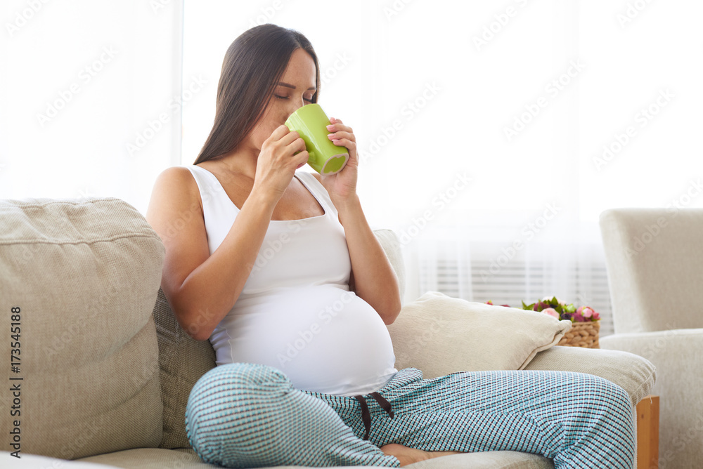 Satisfied pregnant woman tasting tea from mug Satisfied pregnant woman tasting tea from mug