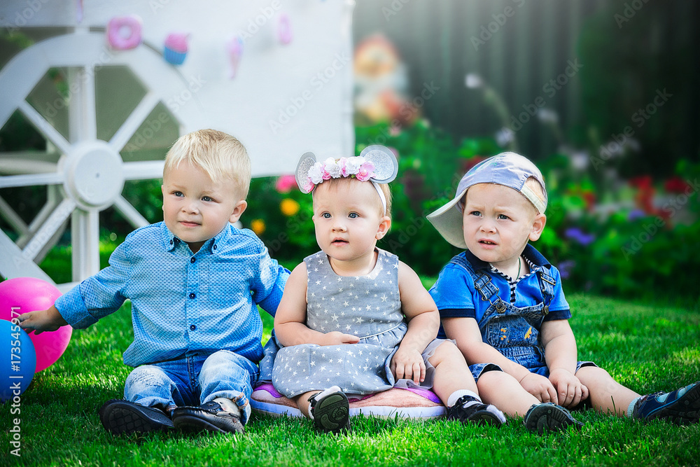 three small children sit on green grass at a children's holiday against the backdrop of candy bar. three small children sit on green grass at a children's holiday against the backdrop of candy bar.