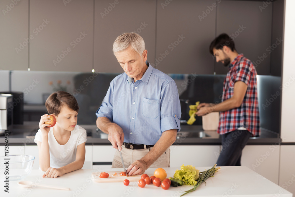 The old man and the boy are busy preparing a salad for Thanksgiving. Behind them, a man washes salad leaves