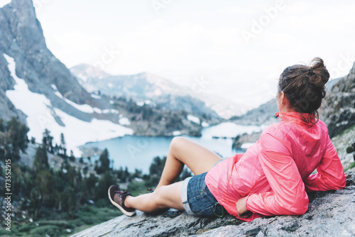 Handsome woman resting high in mountains. Risky rock climbing in peaceful wilderness area. Enjoying amazing snowy lake view