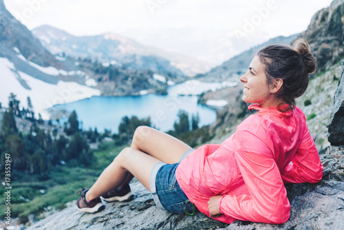 Young woman sitting and resting high in mountains. Risky rock climbing in peaceful wilderness area. Enjoying amazing snowy lake view photo