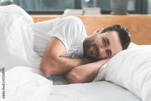 Joyful guy awakes in comfortable bed