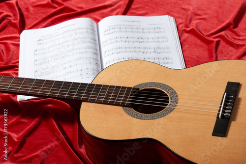 acoustic guitar and music notes on red fabric, close view of objects
