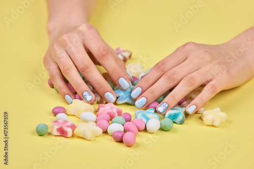 Colorful candies and woman hands. Female hands with beautiful manicure and multicolored candies on yellow background.