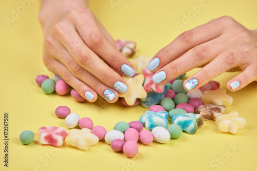 Colorful candies in womans hands. Womans hands with bright manicure taking a colorful candy  yellow background.