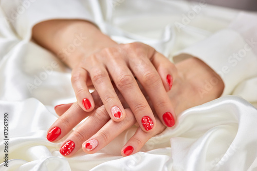 Female romantic design manicure. Young woman well-groomed hands with red patterned nails on white silk. Feminine cleanness and delicacy.