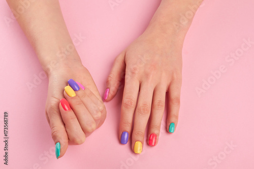 Pastel manicure on female hands. Young woman hands with colorful nail polish on pink table, top view. Nail salon and spa.