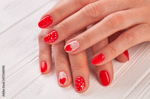 Female hands with polished nails. Woman gentle hands with red hearts and dots design manicure on white wooden background close up.