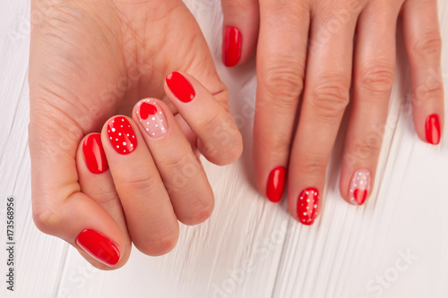 Caucasian woman manicured hands. Valentines Day Holiday bright manicure with painted hearts and dots. Female winter manicure on Valentine Day.