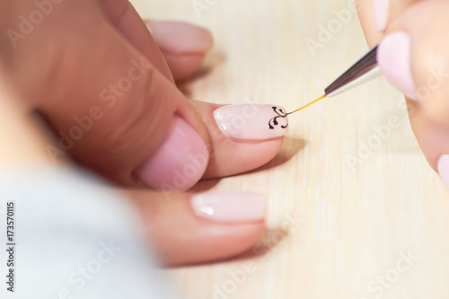 Manicurist drawing on female nails. Nail beautician making a draw on clients nails in beauty salon. Manicur master doing manicure in beauty salon.