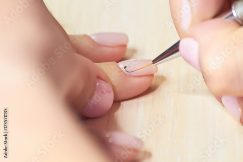 Process of receiving manicure in beauty salon. Manicurist doing design on female nails. Woman having maniure in beauty salon.
