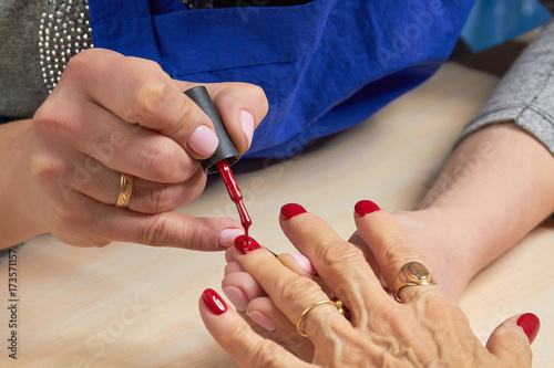Woman applying red varnish to finger nails. The process of painting female nails with red varnish by manicurist in beauty salon.
