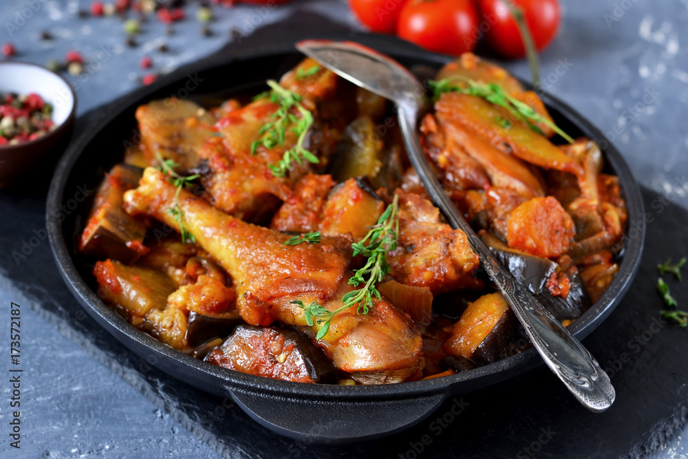 Chicken stewed with vegetables and tomato on a stone board in a frying pan.