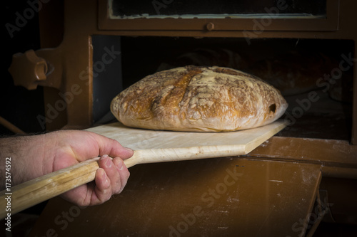 Panadero sacando una hogaza de pan de masa madre del horno tradicional de la panadería