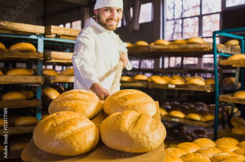 Baker. A young handsome bakery worker on the background of bread, takes bread from a stove with a wooden shovel. Industrial production of bakery products. a man in the baker's special clothing. Bakery