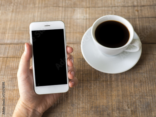 Close up business man's hand holds smart phone with black isolated screen over background of notebook, coffee on wooden background
