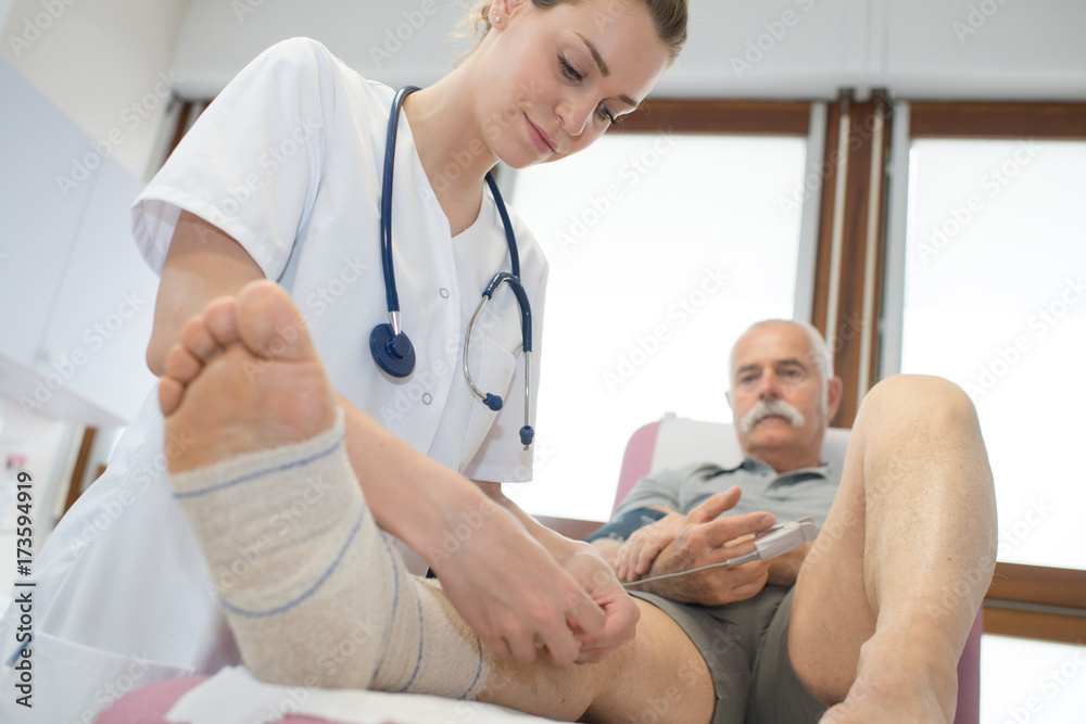 pretty medical doctor is bandaging elder mans broken leg