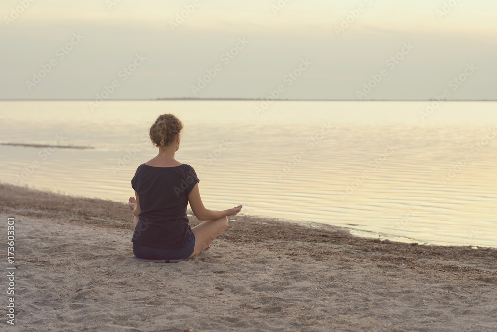 A girl sits on the lake shore and meditates in the evening