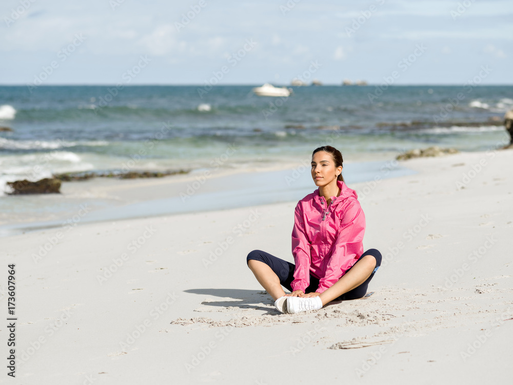 Young woman sitting at the beach in sportswear