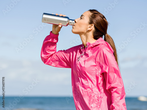 Beautiful girl in sport clothes drinking water after workout on the beach