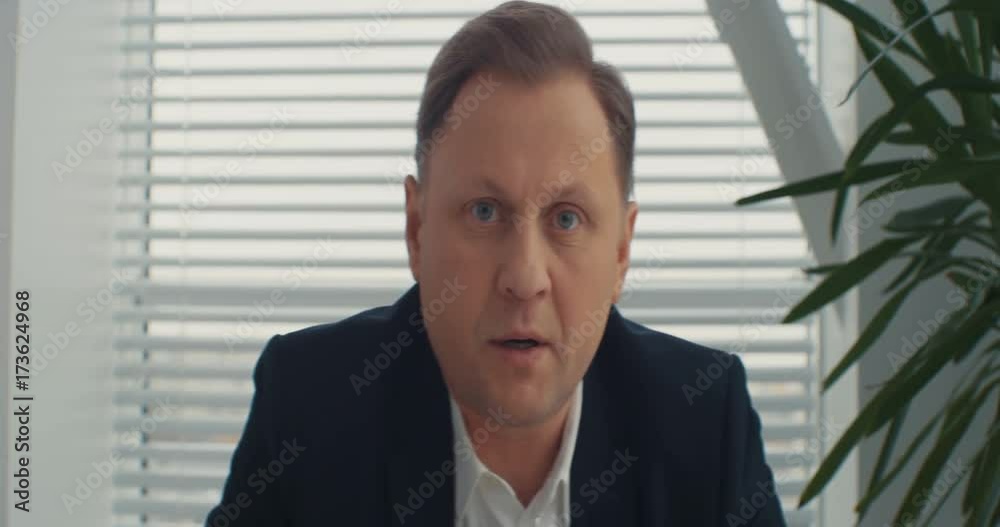 A serious businessman looks at the camera and speaks to the camera in the office. Presentating, talking to camera, presentation, attractive. Shot on RED Epic Camera.