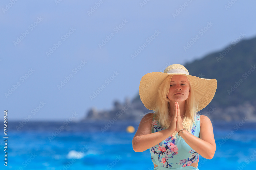 A girl in a blue summer dress with a hat on his head, is on the backdrop of the ocean. And holding palms together. Similan Islands