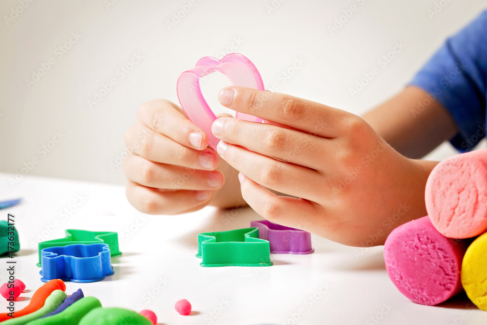 Child hands playing with modeling clay or plasticine on white table Child hands playing with modeling clay or plasticine on white table