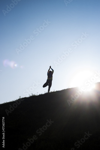silhouette of a girl who engages in yoga on a hill in the background of a blue sky