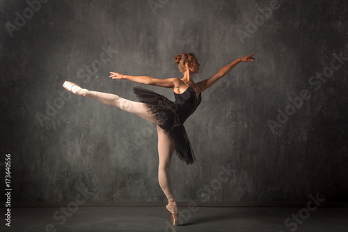 Beautiful attractive blonde woman primer ballerina in a black dance pack, white pantyhose and pointe shoes beautifully dances ballet in a dark studio