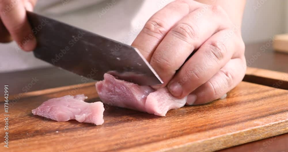 Close up the human hand cutting raw pork on wooden chop board in kitchen room , 4K Dci resolution