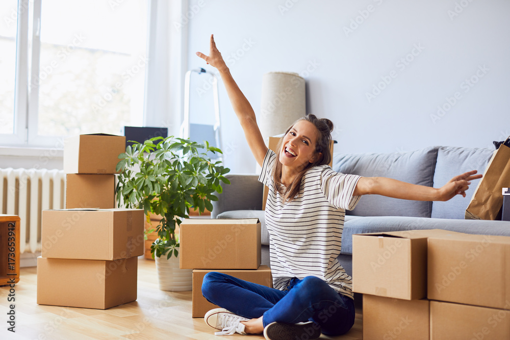 Young woman sitting in new apartment and raising arms in joy after moving in - obrazy, fototapety, plakaty 
