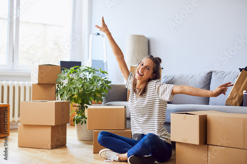 Young woman sitting in new apartment and raising arms in joy after moving in