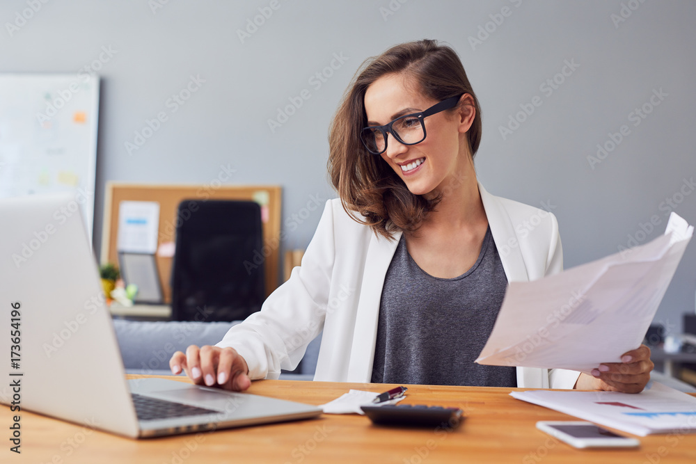 Smiling young woman working in home office using laptop and documents Smiling young woman working in home office using laptop and documents