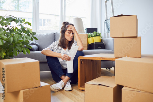 Worried young woman looking at bill sitting on floor in new apartment after moving in photo