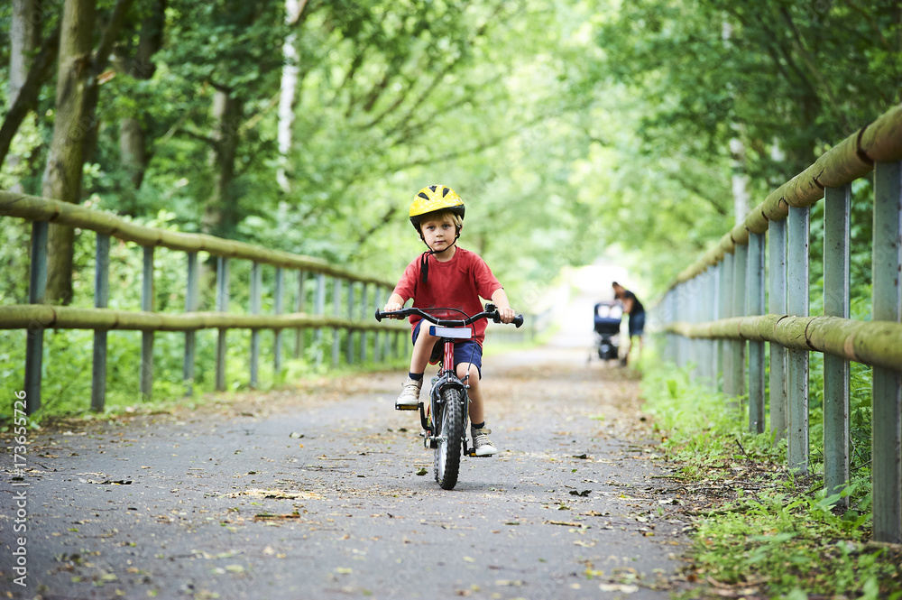 Naklejka premium Child boy on a bicycle on bicycle path in summer. Boy cycling outdoors in safety helmet 