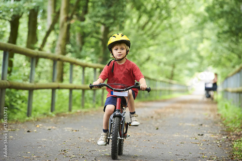 Fototapeta Naklejka Na Ścianę i Meble -  Child boy on a bicycle on bicycle path in summer. Boy cycling outdoors in safety helmet
