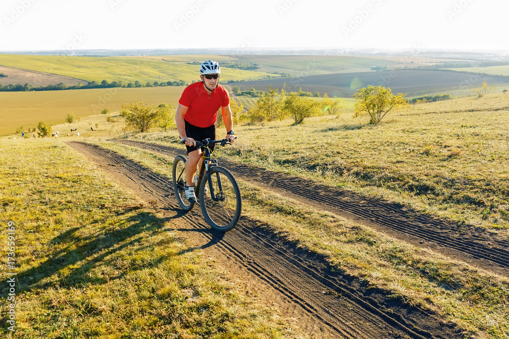 Obraz premium Bike adventure travel photo. Bike tourist rides on the country road. Sunset on background.
