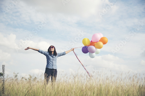 Happy woman holding colorful of balloons on a green meadow with cloudy and blue sky