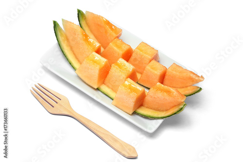Sliced orange melon in pieces on a white plate with wooden fork.