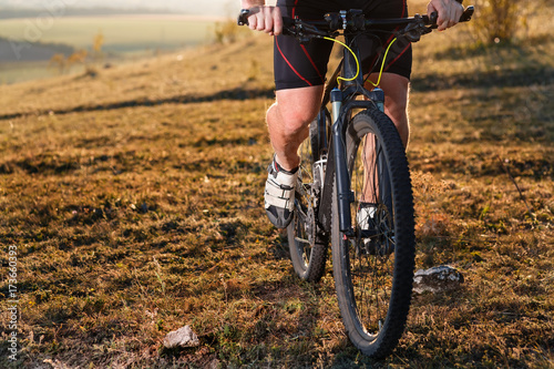 Closeup of cyclist man legs and hands riding mountain bike on outdoor trail in nature