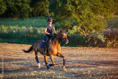 woman riding brown horse wearing helmet in field