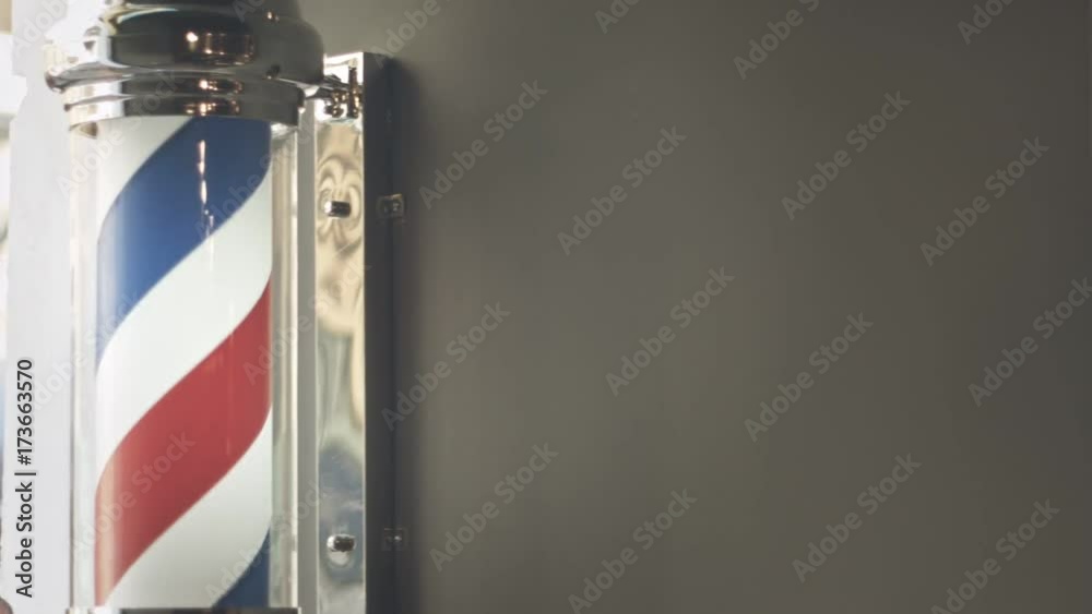 Barber pole rotating on wall in hairdresser shop. Barber pole spinning at barbershop. Vintage barbershop and hairdresser symbol. Traditional barber pole rotating in barbershop. Barber logo