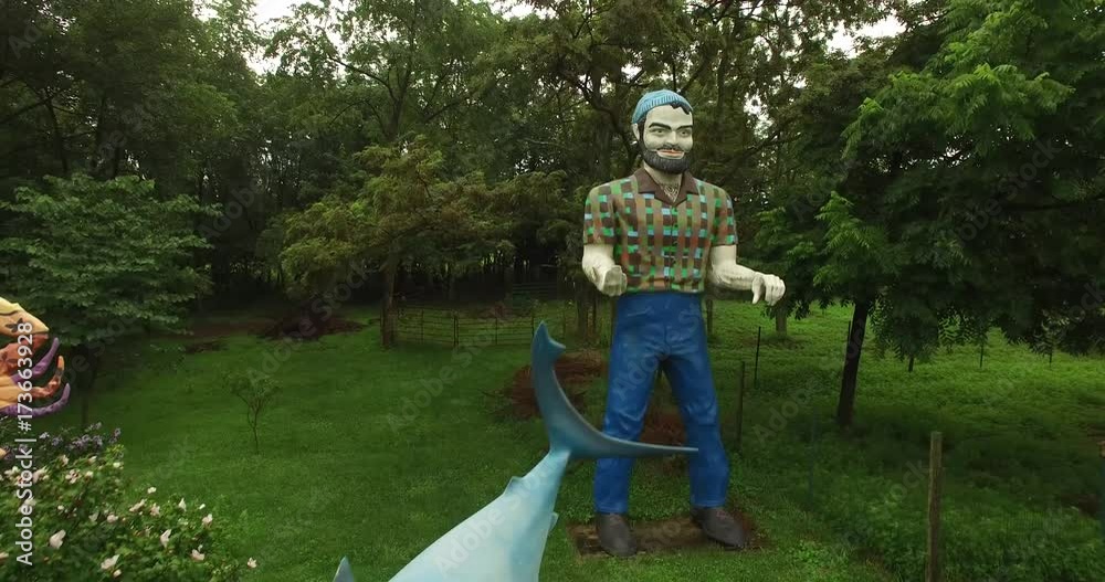 Camera orbiting above Paul Bunyan the muffler man and Finding Nemo shark all set in the countryside.
