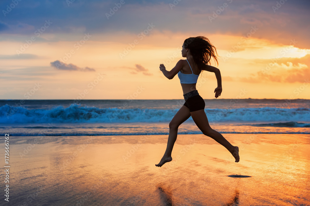 Barefoot sporty girl silhouette running along ocean surf by water pool to keep fit and health. Sunset black beach background with sun. Woman fitness, jogging sport activity on summer family holiday.