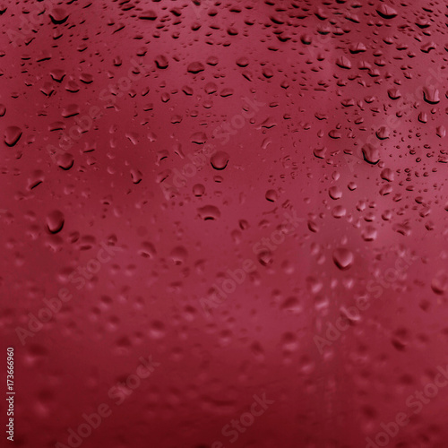 Drops of rain on red glass background. Natural Pattern of raindrops. Rain in the city.